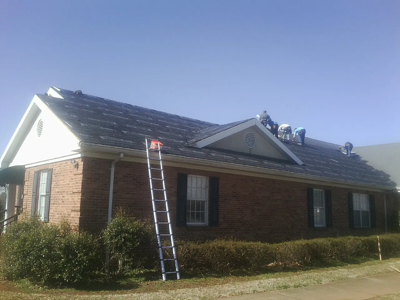 Crew tearing shingles off a brick ranch roof with a ladder set — Metal Roof Repair work by our crew in Ardmore